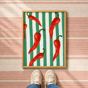 Puede incluir: Una impresión de arte mural rectangular enmarcada que presenta un patrón de chiles rojos brillantes dispersos sobre un fondo de rayas verticales blancas y verde bosque. El marco de madera rodea la obra de arte, que muestra cinco chiles distintos.