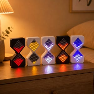 Könnte beinhalten: Fünf LED-Leuchten in Sanduhrform mit unterschiedlichen Farbanzeigen: rot, gelb, lila, orange und blau. Die Lichter sind auf einer Holzoberfläche angeordnet, mit einer Lampe und einer Pflanze im Hintergrund. Die Lichter sind etwa 15 cm hoch.