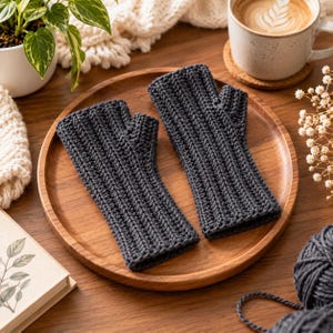 May include: A pair of dark gray fingerless gloves featuring a vertical ribbed crochet pattern. The gloves are constructed with a dedicated thumb opening and a straight cuff design, showcasing a consistent textured stitch throughout the fabric.