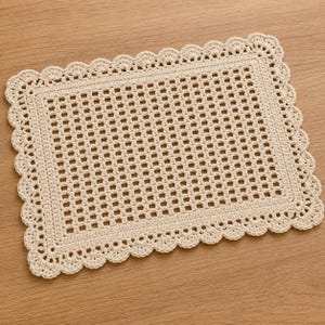 May include: A rectangular off-white crochet doily featuring a central grid pattern composed of small square openings. The piece is finished with a decorative scalloped border consisting of repeating rounded loops along all four edges.