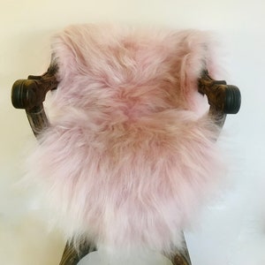 May include: A soft, fluffy pink sheepskin rug with long, white and pink fur. The rug is draped over a wooden chair.