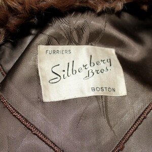 May include: A white label with black text that reads "Furriers Silberberg Bros. Boston" on a brown fur coat.