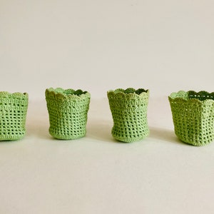 Puede incluir: Cuatro pequeñas cestas de crochet verde con bordes festoneados.