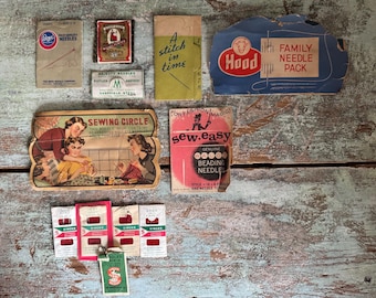 May include: A collection of vintage sewing supplies, including needle packets and a sewing circle advertisement. The items are in various colors, including red, green, and blue, and are arranged on a weathered wooden surface.