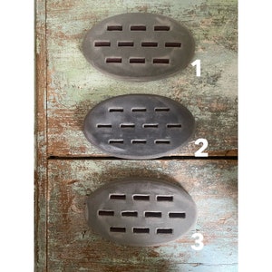 May include: Three oval-shaped, gray cabinet pulls with rectangular cutouts. The pulls are mounted on a distressed, weathered wooden cabinet with a teal and green paint finish. Each pull is numbered 1, 2, and 3.