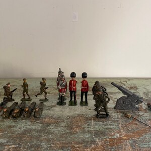May include: A collection of vintage toy soldiers, including a group of red-coated soldiers, green-clad soldiers, and a cannon. The soldiers are made of metal and have a painted finish.