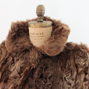 May include: A brown fur coat with a large collar. The coat is on a vintage dress form with the label "Bauman Original Model, New York, Inc."