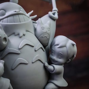 May include: A gray figurine depicting characters from a popular animated film. The central figure is a large, smiling creature with a round body, holding an umbrella. A smaller character clings to its side, and other figures are also present.
