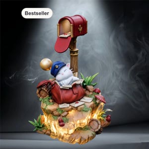 May include: A whimsical figurine featuring a white cat in a blue hat, resting in a red mailbag on a rocky base. A red mailbox and gold sphere are also present. The base is illuminated with warm light, and the word "Bestseller" is displayed.
