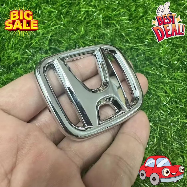 May include: A shiny chrome Honda emblem, held in a hand, against a green background. The emblem is the classic Honda 'H' logo. The image also includes 'BIG SALE' and 'BEST DEAL!' text.