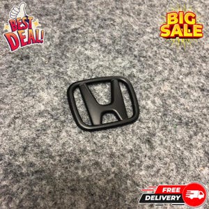 May include: A matte black Honda emblem, featuring the iconic "H" logo, is displayed against a gray textured background. The image also includes "Best Deal!" and "Big Sale" text graphics, along with a "Free Delivery" graphic.