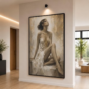 May include: A large framed canvas art print shows a seated figure in a flowing white dress with gold accents. The artwork uses a neutral palette of beige, gold, and brown tones, creating a serene and elegant aesthetic. The painting is displayed in a modern interior setting.