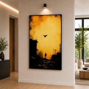 Könnte beinhalten: Gerahmter Kunstdruck, der eine Silhouette einer Person zeigt, die in einer Stadtszene geht. Das Kunstwerk zeigt einen warmen gelb-orangen Sonnenuntergangshimmel mit einem fliegenden Vogel. Die Gebäude sind in dunkler Silhouette dargestellt.