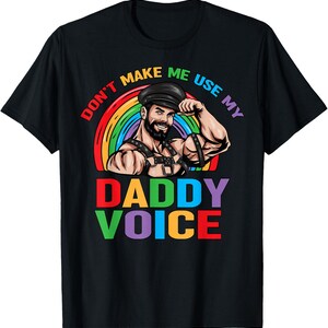 Op de afbeelding: Een zwart t-shirt met een afbeelding van een bebaard persoon met een leren pet en harnas, voor een regenboogboog. De tekst DON'T MAKE ME USE MY DADDY VOICE staat in kleurrijke, dikke blokletters over het ontwerp heen gedrukt.