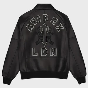 Pode incluir: Casaco de couro preto com gola e punhos canelados. As costas apresentam um design bordado branco com o texto "AVIREX" acima de um emblema estilizado e "LDN" abaixo.