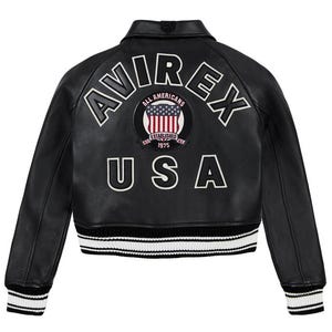 May include: Black leather jacket with white embroidered lettering spelling "AVIREX" and "USA". A circular patch with the American flag and the words "ALL AMERICANS ESTABLISHED 1975" is centered on the back. The jacket has a ribbed collar and cuffs.