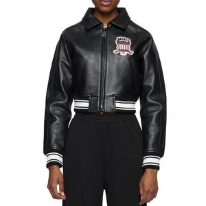 May include: Black leather bomber jacket with a cropped fit. The jacket features a white and black striped hem and cuffs. A patch with the text "AVIREX" and a patriotic design is on the chest.
