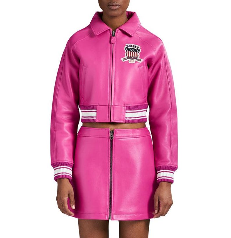 K&ouml;nnte beinhalten: Ein leuchtend pinkfarbenes Lederjacken- und Minirock-Set. Die Jacke hat einen Rei&szlig;verschluss, einen Kragen und einen Aufn&auml;her auf der Brust. Die Manschetten und der Saum der Jacke haben wei&szlig;-rosa Streifen. Der Rock hat einen Frontrei&szlig;verschluss.