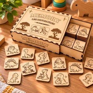 May include: A wooden memory game box with a sliding lid featuring the text MEMORY LES DINOSAURES JEU POUR ENFANTS and engraved dinosaur illustrations. The set includes multiple square wooden tiles with various dinosaur line art designs.