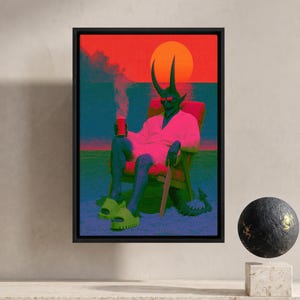 Può includere: Una stampa artistica da parete incorniciata raffigurante una figura dalla pelle scura con corna, occhiali da sole e una vestaglia bianca, seduta su una sedia a sdraio sulla sabbia. La figura tiene in mano una bevanda rossa su un tramonto vibrante.