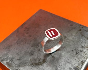 May include: A silver ring with a red square-shaped stone featuring two white parallel lines.