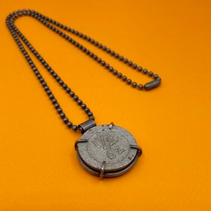 Peut inclure: Un collier en argent avec un pendentif rond sur lequel est inscrit le numéro "120" sur une surface texturée. Le collier est composé d'une chaîne en argent avec un fermoir en argent.