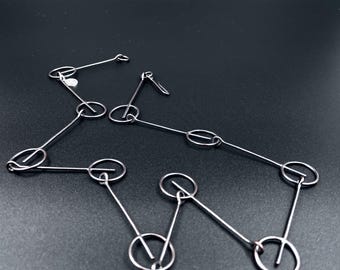 May include: A silver-toned necklace and earrings set. The necklace features a series of connected oval and circular links. The earrings have a similar design, with a single hook. The jewelry is displayed on a dark surface.