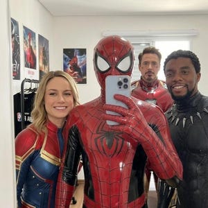 Puede incluir: Un grupo de cuatro personas con trajes de superh&eacute;roes, incluyendo un traje rojo y azul de Spider-Man, un traje rojo y azul de Captain Marvel, una armadura roja y dorada de Iron Man y un traje negro de Black Panther, posando para un selfie.