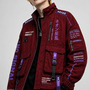 Puede incluir: Una chaqueta utilitaria de color rojo oscuro con cuello alto, múltiples bolsillos y varios estampados gráficos en blanco y morado. La chaqueta incluye textos como "NO SIGNAL", "NEON REBELLION" y "BTS-ARMY", junto con largas correas moradas colgando.