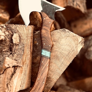 May include: A hand axe with a polished silver-toned metal blade and a dark brown wood handle. The handle features a curved shape with small metal pins and a central inlay band of light blue material with a subtle pattern. The axe head is sharp.