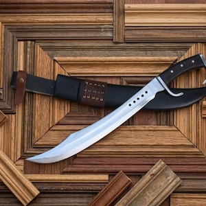 May include: A curved steel blade with a series of five circular cutouts near the hilt, featuring a dark handle with silver rivets and a matching black leather sheath with brown leather accents and lacing details along the scabbard body.