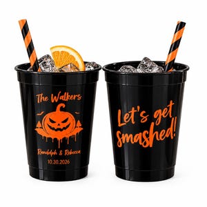 May include: Two black plastic cups filled with ice and orange slices, each featuring orange text and graphics. The left cup displays a pumpkin, 'The Walkers', 'Randolph & Rebecca', and '10.30.2026'. The right cup reads 'Let's get smashed!' with striped straws.