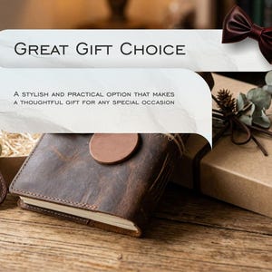 Op de afbeelding: Een leren notitieboek, sleutelhanger en geschenkdoos zijn gerangschikt op een houten oppervlak. Het notitieboek is bruin met een ronde sluiting. De sleutelhanger heeft een initiaal. De geschenkdoos is vastgebonden met touw. Tekst: "Great Gift Choice."