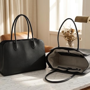 May include: Two black leather tote bags are displayed on a marble surface. One is closed, the other open, showing a light-coloured interior. Both bags have long handles and a structured design, ideal for daily use.