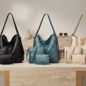 May include: A selection of handbags and smaller bags in black, teal, and cream. The bags are arranged on a light-coloured surface, against a neutral backdrop. The handbags feature long straps and multiple compartments.