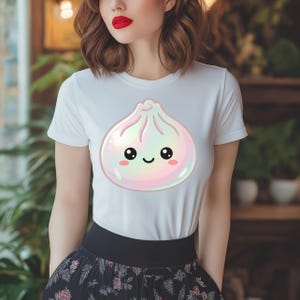 May include: White t-shirt featuring a cute, cartoon-style dumpling with a smiling face. The dumpling has a pearlescent, iridescent effect with pink and purple hues. The shirt is a classic crew neck style.