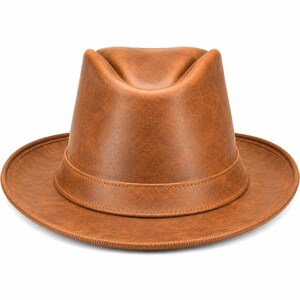 Pode incluir: Um chapéu fedora castanho médio com uma textura lisa semelhante a couro. O chapéu apresenta uma coroa vincada, uma aba estruturada e uma faixa tonal a condizer que envolve a base da coroa. A superfície tem uma subtil variação de cor.