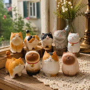 Puede incluir: Una colección de nueve pequeñas figuras de gatos talladas a mano en madera con diversos colores y patrones, incluyendo naranja, tricolor, blanco y negro, gris atigrado y blanco con collares rojos y pequeñas campanas doradas.