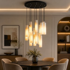May include: A contemporary chandelier featuring multiple cylindrical lights suspended from a black ceiling plate. The lights are a creamy white, emitting a warm glow. The chandelier hangs above a dark round table in a dining room setting. The lights are approximately 30 cm in length.