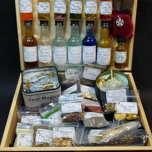 May include: A wooden box containing an assortment of 15 ml glass bottles filled with coloured oils and waters, a metal ankh, a small red pouch with a pentacle charm, two candles labelled Seer Magick, and various small plastic bags of herbs and resins.