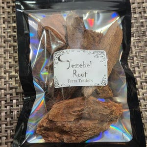 May include: A clear, resealable plastic pouch with a black border containing several pieces of brown, textured Jezebel Root. A white rectangular label on the front features the text Jezebel Root and Terra Traders with decorative star and moon graphics.
