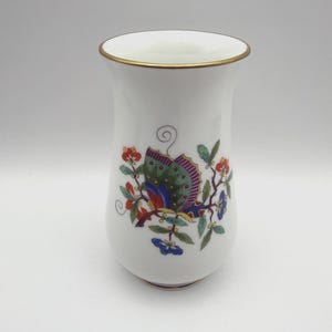 May include: A white porcelain vase with a flared rim and a gold-toned edge. The body features a colorful graphic of a butterfly with green, blue, and red wings perched on a branch with small orange and blue flowers and green leaves.