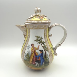 Könnte beinhalten: Eine Kaffeekanne aus Porzellan mit einer handgemalten Szene von zwei Figuren in einer Landschaft. Die Kanne hat einen gelb-weißen Körper mit goldenen Verzierungen, einen geschwungenen Henkel, einen Ausguss und einen Deckel mit Blütenknauf.