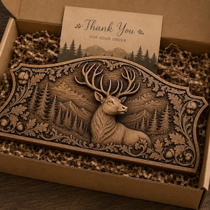 Puede incluir: Placa de madera tallada que representa un ciervo en un paisaje forestal, presentada dentro de una caja de cart&oacute;n con una tarjeta de "Gracias por tu pedido". La placa est&aacute; rodeada de elementos decorativos y material de embalaje.