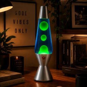 May include: A lava lamp featuring a silver metal base and cap with a clear glass vessel containing blue liquid and bright green wax blobs. The lamp has a conical shape and a small circular red logo on the front of the silver base section.