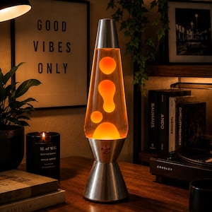 May include: A lava lamp with a conical glass vessel containing orange wax blobs suspended in a clear liquid, set upon a brushed silver metal base and topped with a matching silver cap, emitting a warm glow from the internal light source.
