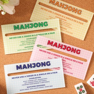 May include: Four rectangular acrylic Mahjong reference cards in yellow, green, pink, and blue with a gingham pattern. Each card features the text MAHJONG, rules about jokers, Charleston instructions, and matching dragons in dark ink.