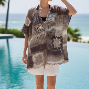 May include: A loose-fitting, short-sleeved crochet poncho featuring a gradient of brown, beige, and white tones. The garment is constructed from a mix of solid mesh panels and intricate floral-patterned square motifs, finished with a scalloped edge.