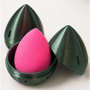 May include: A pink beauty blender sponge inside a dark green case. The case is open, revealing the sponge. The text "PERFECT FIT" and "Fits most standard beauty blender sponges" is visible. Dimensions: 2.75 in (H) x 2.1 in (W).