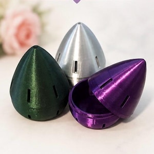May include: Three beauty blender travel cases in green, silver, and purple. The purple case is open, revealing the interior. The cases are bullet-shaped with ventilation slots. Text on the image reads: BEAUTY BLENDER TRAVEL CASE.